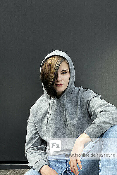 Teenage girl in hooded shirt sitting against gray background