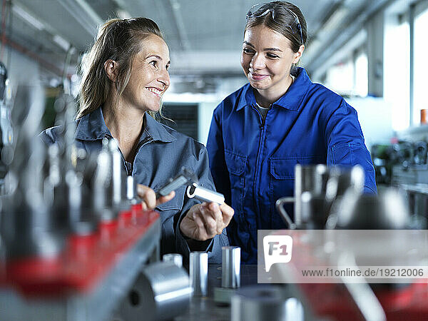 Smiling industry worker teaching trainee to measure CNC tool in factory