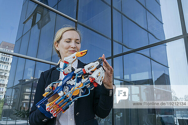 Smiling female architect examining robotic arm near office building