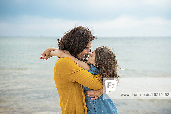 Happy woman embracing daughter in front of sea at beach