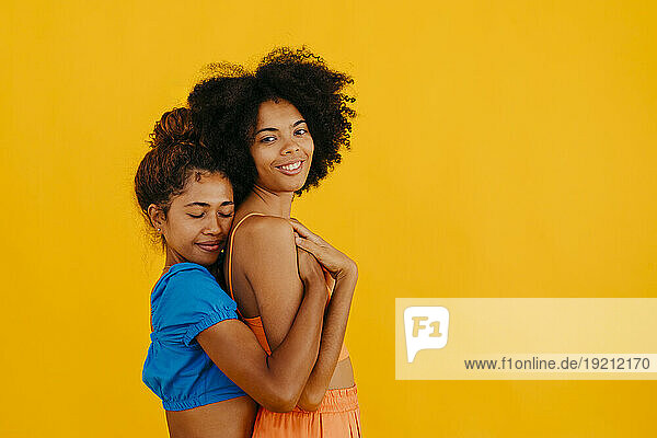 Woman with eyes closed embracing friend against yellow background