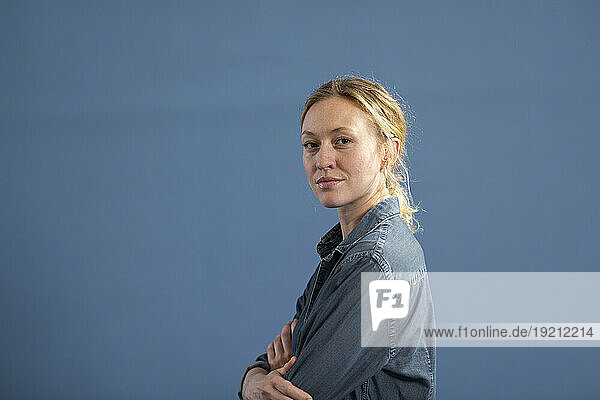 Blond woman with arms crossed against blue background