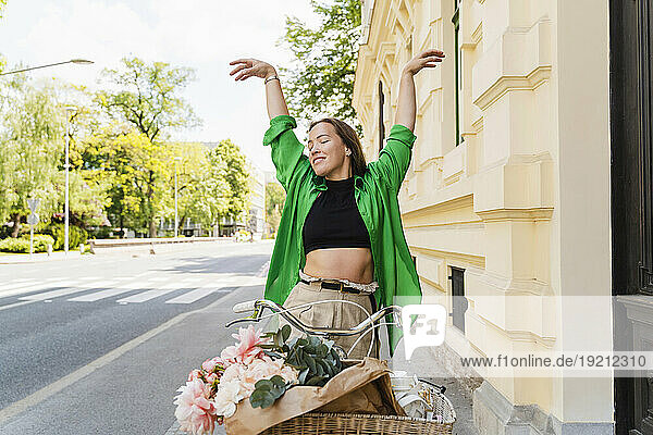 Happy woman with bicycle and arms raised on street
