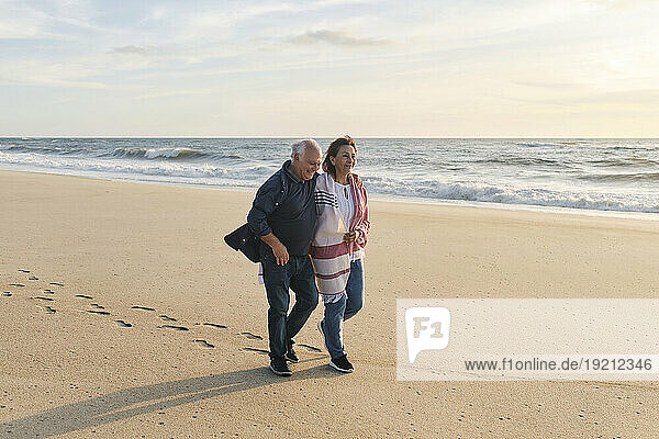 Happy senior couple walking on sand at beach