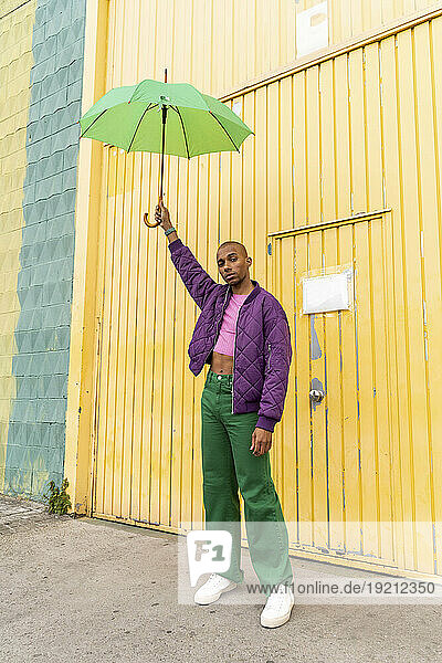 Non-binary person holding umbrella in front of yellow shutter door
