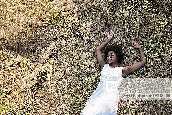 Young woman with eyes closed relaxing on dry grass in field