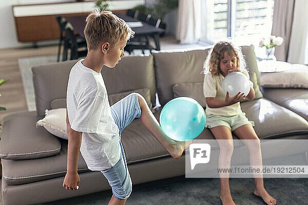 Siblings playing with balloons in living room at home
