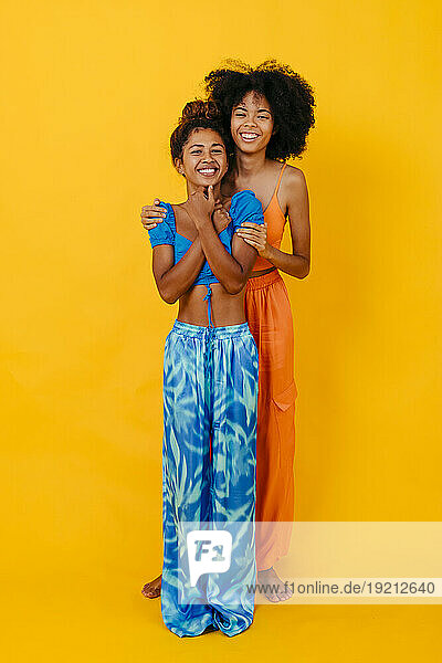 Happy multiracial friends standing against yellow background