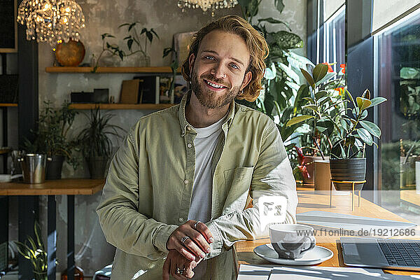 Smiling young businessman leaning on table at cafe