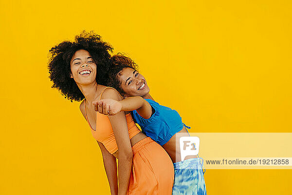 Carefree woman leaning on friend against yellow background