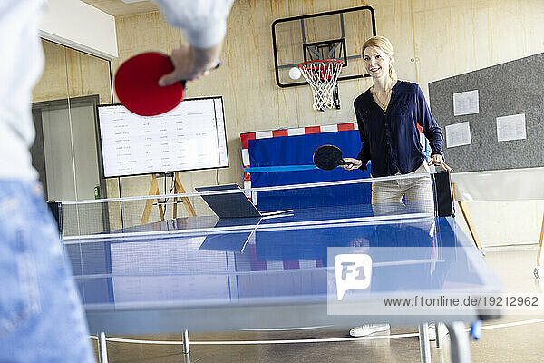 Smiling Businesswoman playing tennis with colleague in modern office