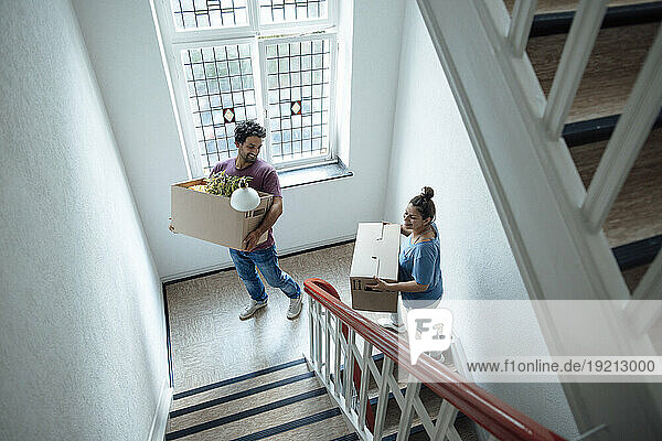 Happy man and woman with cardboard boxes moving up on staircase