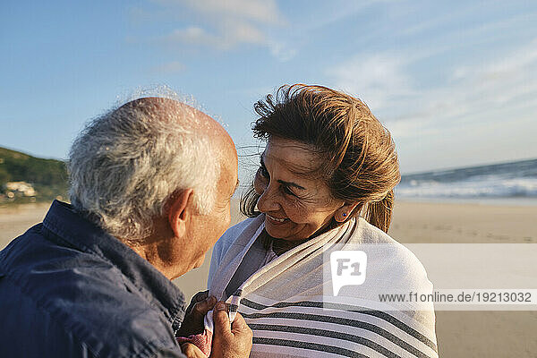 Happy senior man and woman looking at each other under cloudy sky
