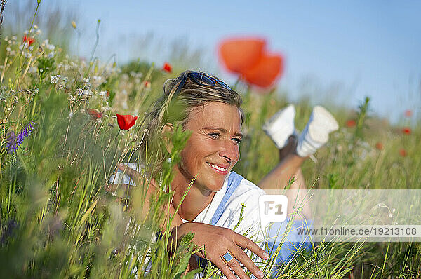Smiling woman lying down amidst flowers in meadow