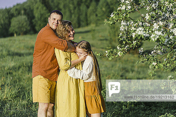 Parents and daughter hugging on grass in meadow