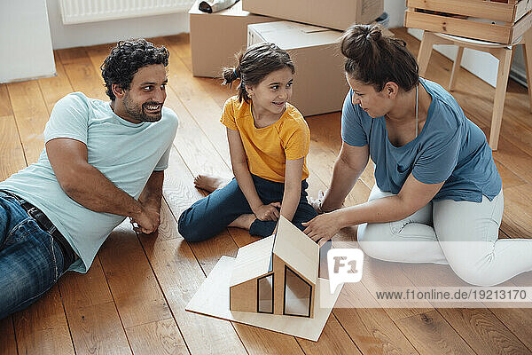 Happy family sitting with model house on floor at home