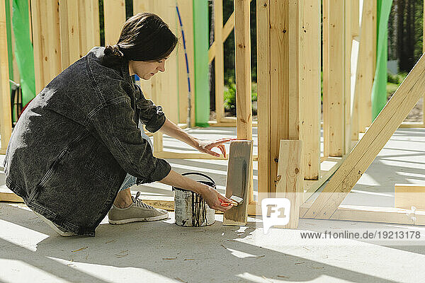 Blue-collar worker painting plank with paintbrush at construction site