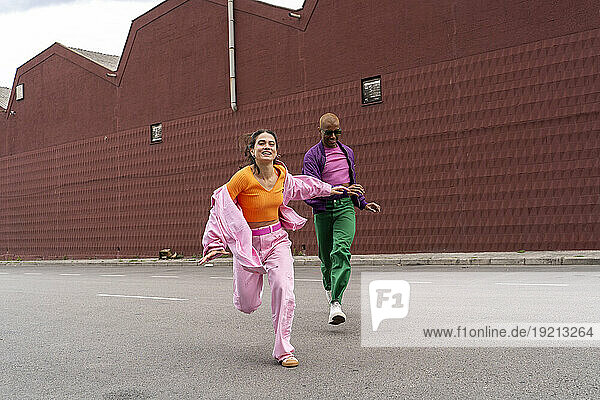 Cheerful woman running and having fun with friend in front of building