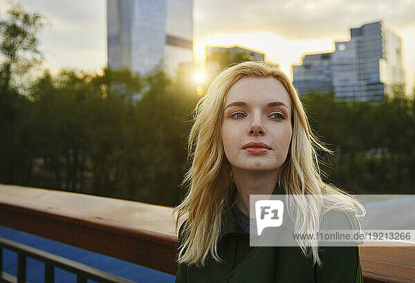 Contemplative woman standing by railing at sunset
