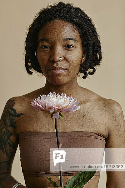Young woman with acne scars holding flower against brown background