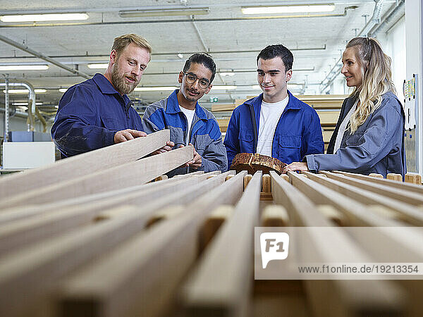 Carpenter holding wooden plank and explaining trainees in factory