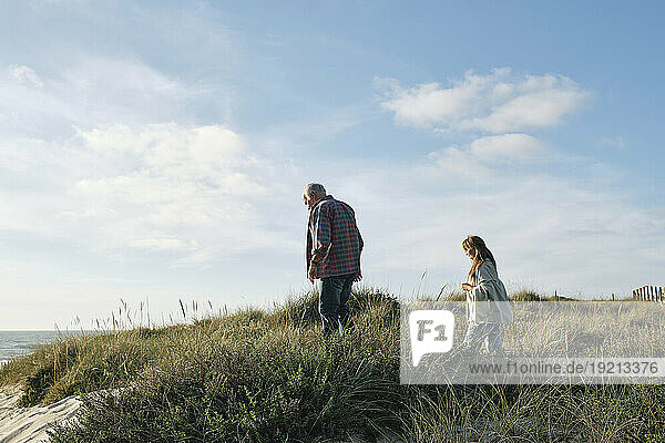 Senior man and woman walking amidst plants at beach on sunny day