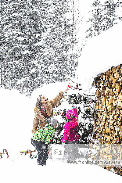 Grandmother and siblings decorating Christmas tree in snow