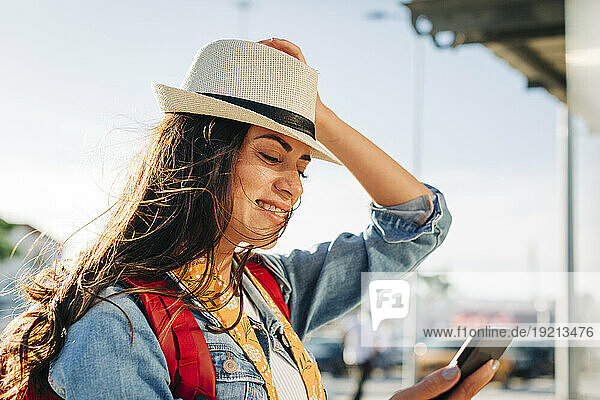 Happy young woman with hat using mobile phone