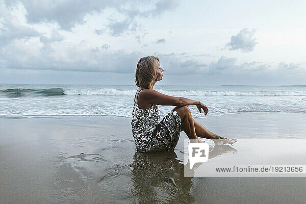 Contemplative woman sitting at beach under sky