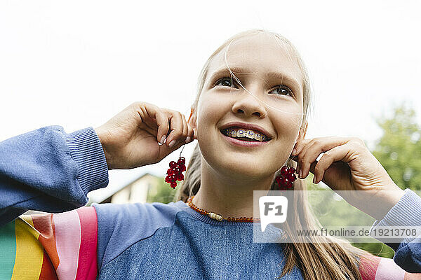 Smiling girl holding fresh redcurrants near ears