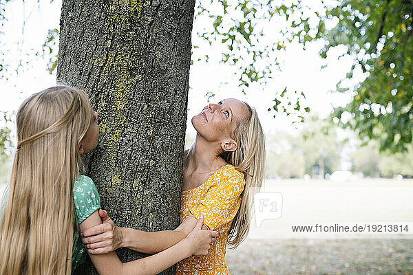 Mother and daughter hugging tree trunk in park