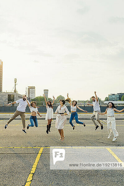 Cheerful friends jumping together and having fun on road under sky