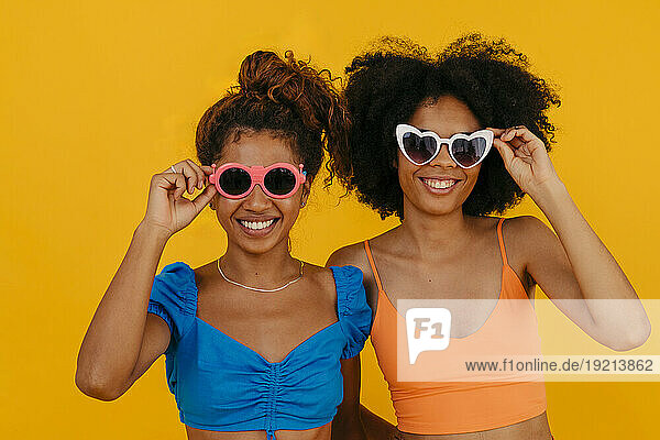 Happy women wearing sunglasses against yellow background