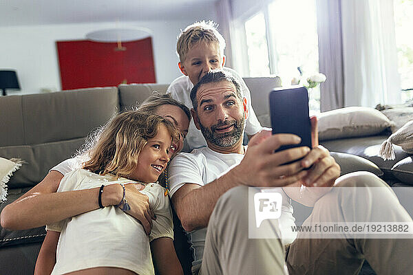 Mature man taking selfie with family on mobile phone at home