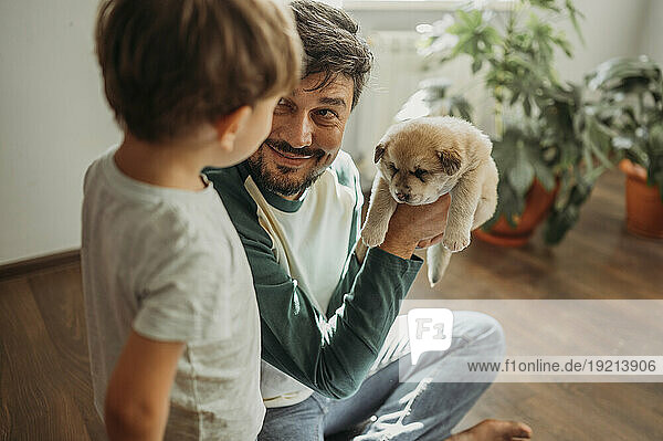 Smiling man showing cute puppy to son at home