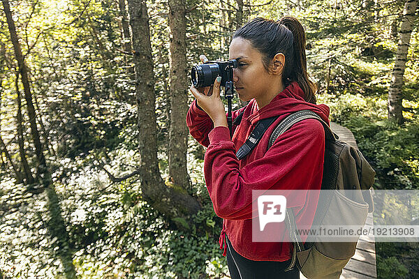 Young woman photographing with camera standing in forest