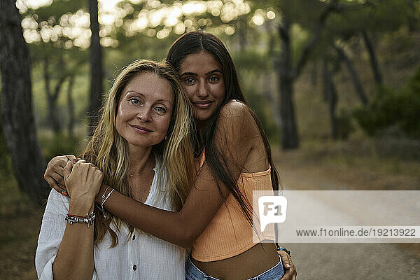 Smiling teenage girl hugging mother in forest