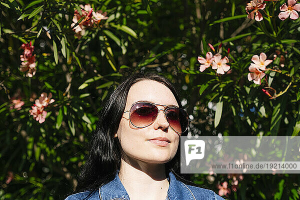 Young woman wearing sunglasses near flowering plants on sunny day
