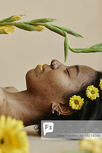 Young woman with yellow flowers on hair relaxing against brown background