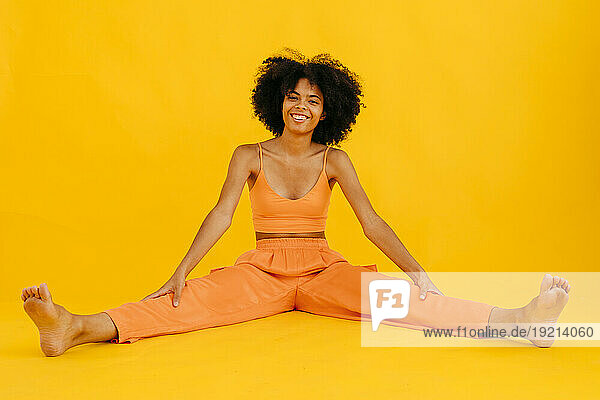 Smiling woman spreading legs against yellow background