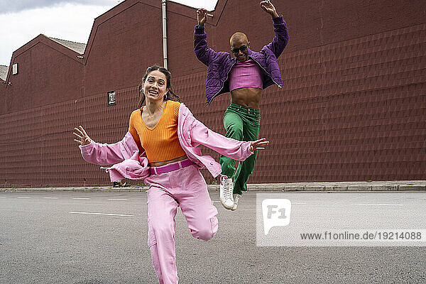 Cheerful woman dancing with friend jumping in front of building