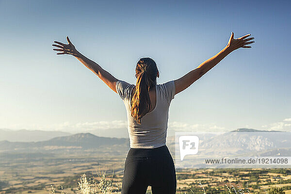 Young woman with arms outstretched standing in front of sky