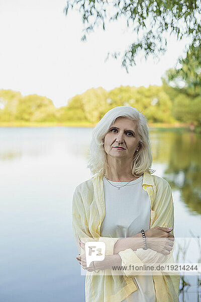 Mature woman with white hair hugging self in front of lake