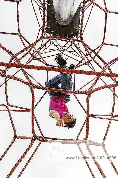 Woman hanging on jungle gym under sky