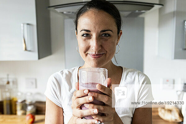 Happy woman holding glass of milkshake at home