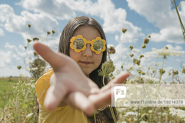 Girl with flower sunglasses gesturing in field