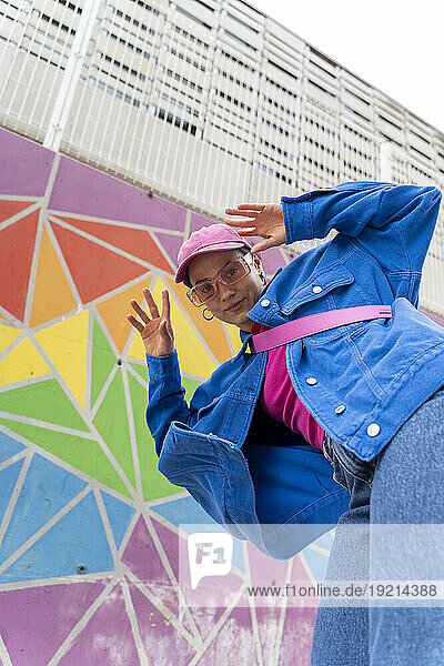 Hip woman with blue jacket gesturing in front of colorful wall