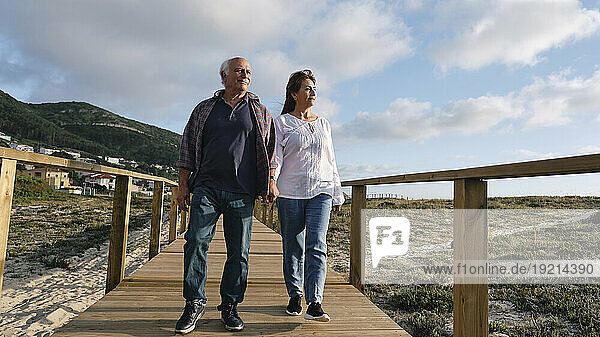 Smiling woman and man holding hands walking on boardwalk