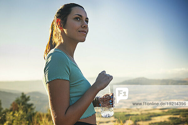 Beautiful woman holding water bottle on sunny day