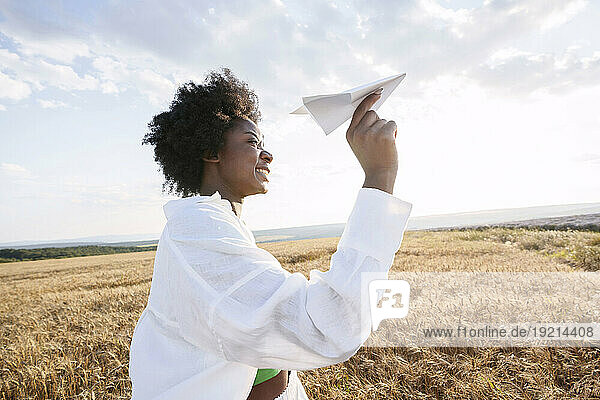 Happy woman with curly hair holding paper plane in field